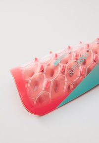 Pièce d'équipement de protection de forme hexagonale de couleur rose, avec des accents en relief et une section turquoise, indiquant la fonctionnalité "Superlock".