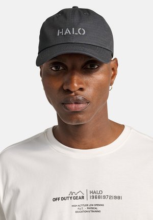 Mörkgrå basebollkeps med broderad text "HALO" i ljusgrått; har en böjd skärm och tygstruktur, bärs av en person med medium hudton.
