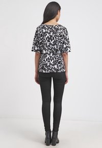 Top grafico in bianco e nero con lettere in grassetto e forme astratte, maniche corte e vestibilità ampia, abbinato a jeans skinny neri.