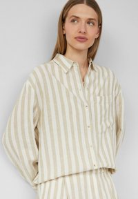 Lniany, beżowy button-down w poziome paski w kolorze kremowym, z kieszenią na piersi i miękkim, luźnym krojem oraz podwiniętymi rękawami.