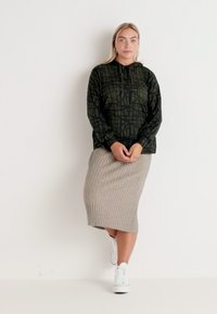 Črna kapuca s geometrijskim zelenim vzorcem, z vrvico na vratu. Svetlo siva rebrasta midi krila, bele superge. Preprost, sproščen outfit.