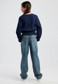 Navy textured long-sleeve top with a loose fit, paired with light blue wide-leg denim jeans. Soft fabric with a gathered waistband detail.