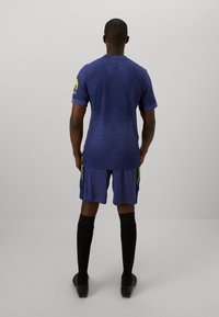 Marine sportshirt met ribbeltextuur, korte mouwen en gele accenten op de mouwen en zijden, gecombineerd met bijpassende shorts en zwarte sokken.