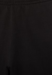 Közeli kép egy fekete elasztikus derékpántjáról és a sima fekete nadrág vagy leggings anyagának textúrájáról.