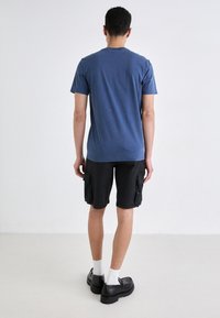Blue cotton t-shirt paired with black cargo shorts. Features a standard fit, short sleeves, and side cargo pockets, worn with black shoes.