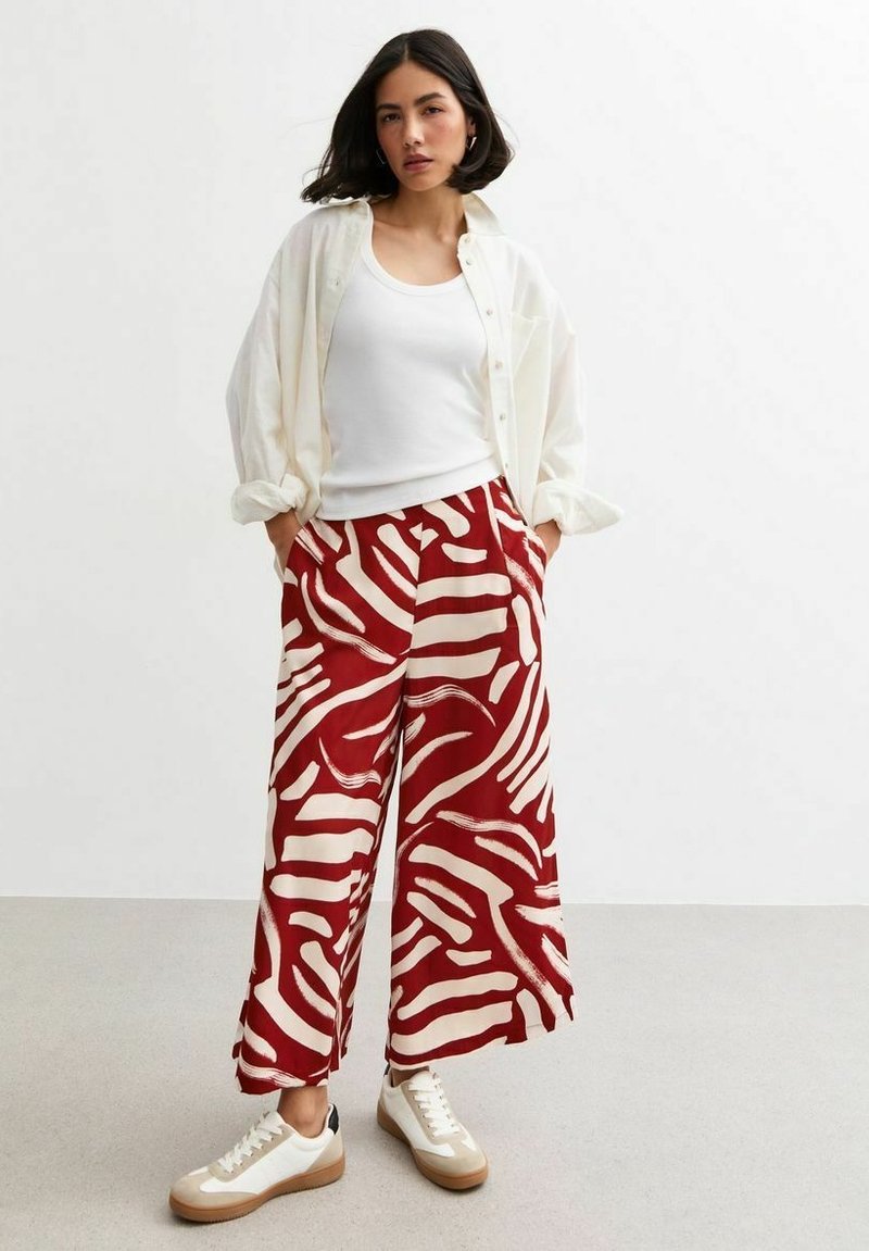 Red and white patterned wide-leg pants paired with a white tank top and oversized button-up shirt, alongside white sneakers with a beige sole.