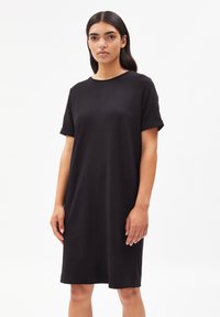 Robe t-shirt en coton noir avec des manches courtes, coupe décontractée, encolure ronde et ourlet au niveau des genoux. Texture lisse et détails de design minimalistes.