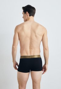 Black boxer shorts with a gold elastic waistband, fitted design, smooth texture, and no visible branding or patterns, viewed from the back.