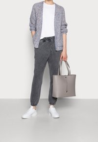 Světle modrý pletený kardigan s texturou, bílý tričko, šedé tepláky, šedá kabelka a bílé tenisky. Kardigan má volný střih a spadlé ramena.