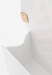 Interno di una borsa bianca con una texture liscia, bordi curvi e dettagli in hardware dorato. Presenta una piccola tasca con una fodera a motivo.