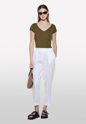 Haut ajusté vert olive en V associé à un pantalon en lin blanc, accessoirisé d'un sac en filet et de sandales noires avec une boucle.