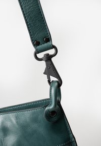 Cinghia per borsa in pelle turchese con finitura testurizzata, dotata di un gancio in metallo nero e cuciture a contrasto, che evidenziano il suo design durevole.