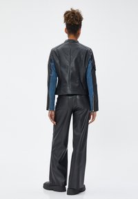 Schwarze Lederjacke mit blauen Jeansärmeln, Reißverschluss-Manschetten und strukturierten Details. Kombiniert mit hochtaillierten, weit geschnittenen schwarzen Hosen.