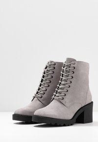 Botas de tobillo de ante gris con diseño de cordones, tacón cuadrado y suela resistente; presentan costuras sutiles y una textura suave.