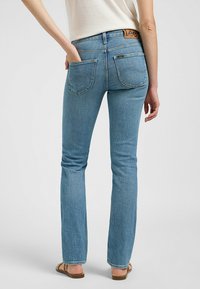 Jeans de denim azul claro con corte recto, bolsillos traseros cosidos y una etiqueta de cuero marrón en la cintura.