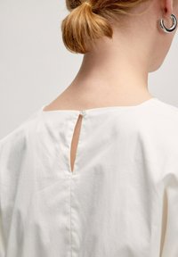Witte katoenen top met een vierkante halslijn en een kleine knoopsluiting op de rug, met een sleutelgaatje net onder de halslijn.
