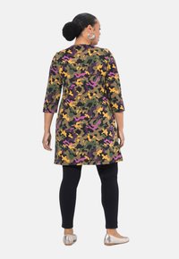 Multicolore camouflage tuniek met driekwart mouwen, in tinten groen, paars en geel. Gepaard met zwarte leggings en zilveren ballerina's.