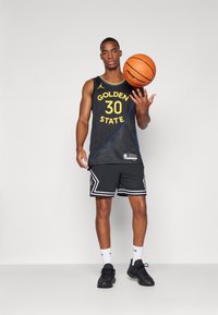 Sort basketballtrøje med gul tekst "GOLDEN STATE 30," mesh tekstur, parret med sorte shorts med hvide accenter og mønstre.
