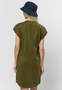 Rochie scurtă, de culoare verde măsliniu, cu mâneci scurte și o croială lejeră, talie strânsă și tiv rotund. O pălărie neagră de tip bucket completează ținuta.