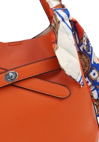 Oranje leren handtas met textuur, versierd met een decoratieve sjaalaccent met een bedrukt ontwerp, afgesloten met een zilverkleurige drukknop.