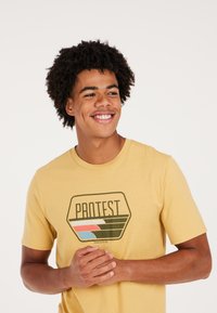Geel katoenen T-shirt met een vintage-stijl "PROTEST" graphic met groene, roze en blauwe accenten. Korte mouwen en een ronde hals.