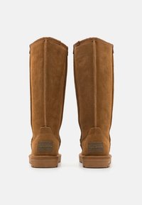 Botas altas de ante marrón con un acabado suave, que presentan un parche con el logo en el talón y costuras verticales para darle estructura. Suela de goma para mayor tracción.