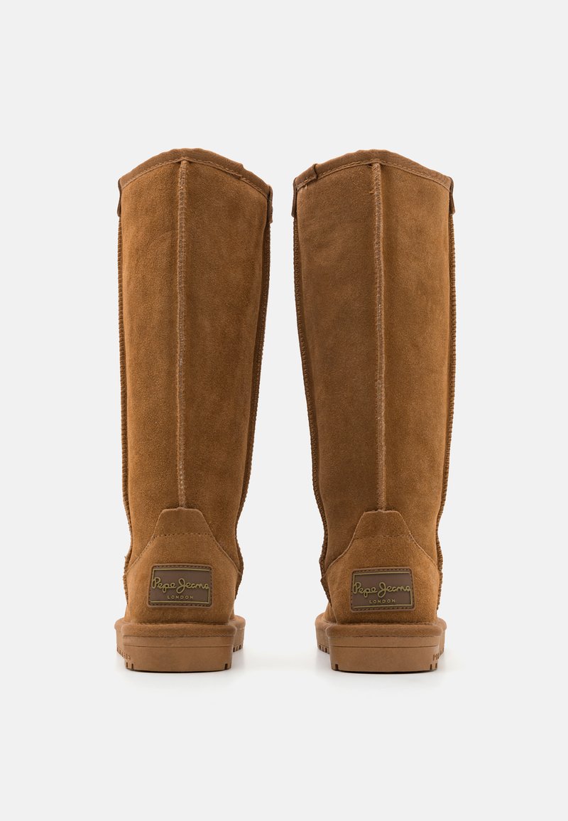 Bottes hautes en daim marron avec une finition lisse, dotées d'un logo cousu au talon et de coutures verticales pour la structure. Semelle en caoutchouc pour une meilleure adhérence.