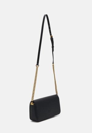 Bolso de hombro de piel negra con cadena dorada y correa negra ajustable sobre un fondo liso y claro.
