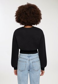 Felpa nera cropped con maniche lunghe e orlo a costine, abbinata a jeans in denim leggero a vita alta di colore azzurro con tasche posteriori.
