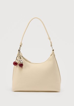 Geantă de mână de culoarea cremei, cu suprafață texturată, o singură curea de umăr și accesoriu cu fermoar în formă de cireșă pe un fundal simplu.