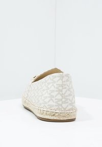 Espadrille blanca con una parte superior de tela texturizada que presenta un patrón geométrico, una suela intermedia de yute y un diseño de punta redonda.