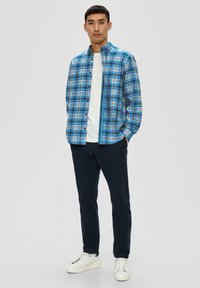 Chemise à carreaux bleue et noire à boutons, t-shirt à col rond blanc en dessous, pantalon marine et baskets blanches. Look décontracté, en coton.