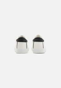 Hvite casual sko med svarte hælakker, glatt lær øvre, hvit gummisåle, minimalistisk design, og diskret logodetalj på hælen.
