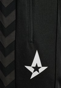 Zwarte sportbroek met een rits, voorzien van een chevronpatroon in een donkerder zwart tint en een wit sterrenlogo op het onderbeen.