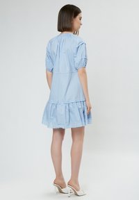 Helles blauen Baumwollkleid mit kurzen Puffärmeln und einem gestuften, rüschierten Saum. Verfügt über eine Spitzenborte am unteren Rand. Getragen mit weißen Absatzschuhen.