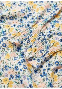Tissu blanc avec un petit imprimé floral jaune, bleu et rose et un détail élastique froncé au niveau du poignet de la manche.