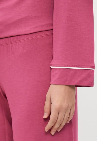 Ružová súprava na voľný čas obsahujúca top s dlhými rukávmi a zaobleným spodným okrajom a nohavice s elastickým pásom; obe vyrobené z hladkej látky.