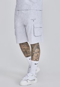 Shorts cargo en coton gris avec poches latérales et un détail de logo. Portés avec des chaussettes blanches et des baskets, avec des tatouages de jambes à motifs.