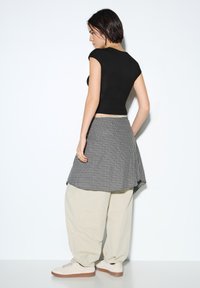 Sort tætsiddende top, grå ternet omslagsnederdel, beige løse bukser og lyse sneakers. Glat stof, ternet mønster, korte ærmer.