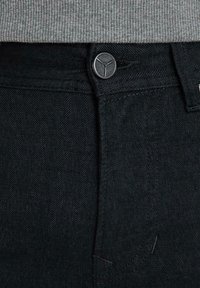 Los pantalones vaqueros de estampado de espiga negra presentan un cierre de botón, una tela ligeramente texturizada y una cinturilla estándar con sutiles detalles de costura.
