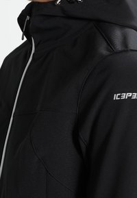 Veste noire zippée avec col montant, tissu texturé, coutures contrastées et logo blanc sur l'épaule. Dotée d'une capuche réglable.