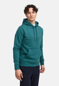 Sudadera color aguamarina hecha de tejido suave, con un bolsillo tipo canguro, capucha con cordón y acento de logo en el pecho. Ajuste estructurado y cómodo.