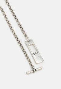 Colar de corrente prateada com um pendente retangular com uma seção aberta e a inscrição "ICON". Superfície texturizada e acabamentos polidos.