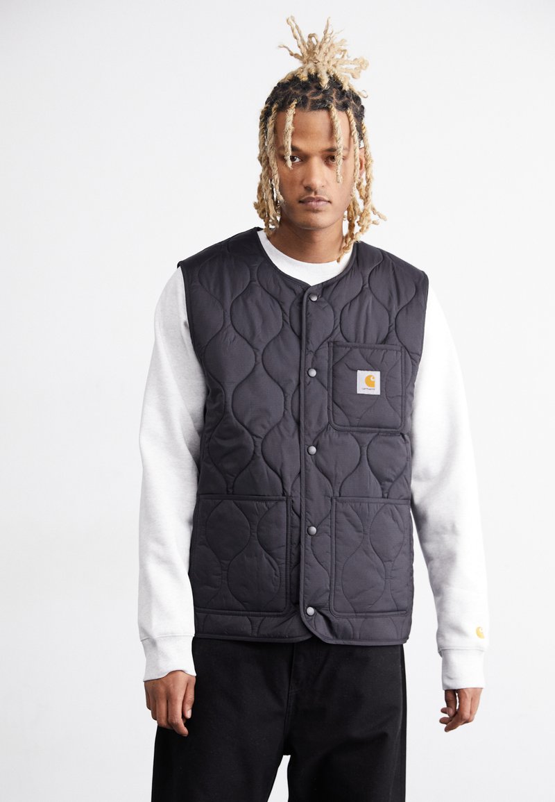 Black quilted vest with a stand-up collar, snap buttons, and a front pocket, worn over a gray sweatshirt, paired with dark pants.