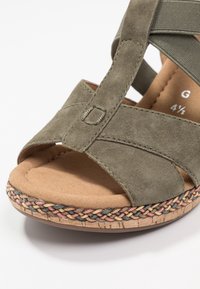 Sandaalit oliivinvihreää mokkaa, jossa on punottu monivärinen reunus, pehmustettu vaaleanruskea pohja ja joustava hihna, koko merkitty sisäpuolelle 4½.