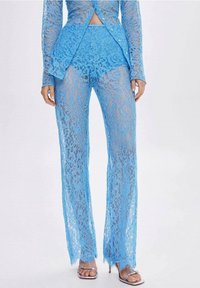 Blauwe kant tweedelige outfit met een lang mouw, peplum-top en wijde broek. De stof heeft een bloemenpatroon en een semi-doorzichtige textuur.