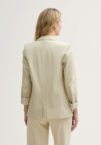 Lichtbeige op maat gemaakte blazer met een gladde textuur, ingeknipte revers en lange mouwen opgerold. Voorzien van een split aan de achterkant.
