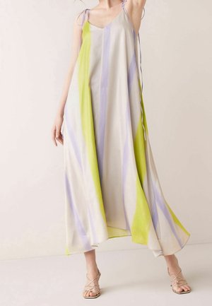 Mujer con un vestido sin mangas y fluido con rayas verticales anchas en amarillo pálido, lavanda y crema, combinado con tacones beige de tiras.