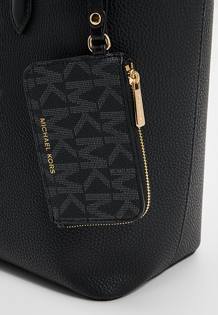 Zwarte leren tote bag met textuur, voorzien van een logo-geprint kaartjeshouder met gouden hardware en ritsdetails aan de voorkant.