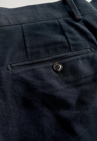 Jūriniai vilnoniai kelnės su užpakaline kišene ir juodu mygtuku. Audinys yra minkštas ir turi lygų, šiek tiek šukuotą paviršių.